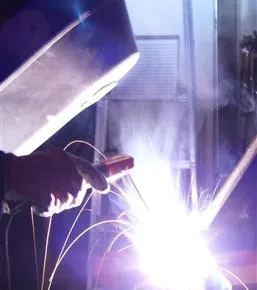 A person welding in an industrial setting with smoke.