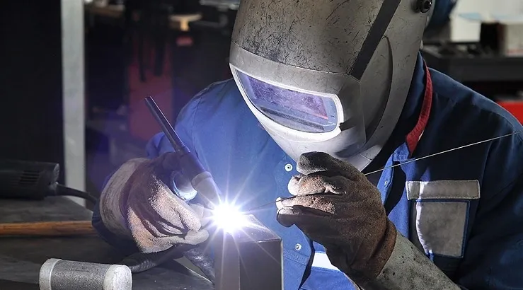 A man welding with a mask on and gloves.